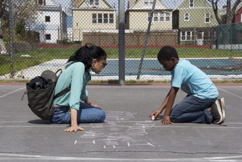 A boy writes haiku on the pavement with chalk