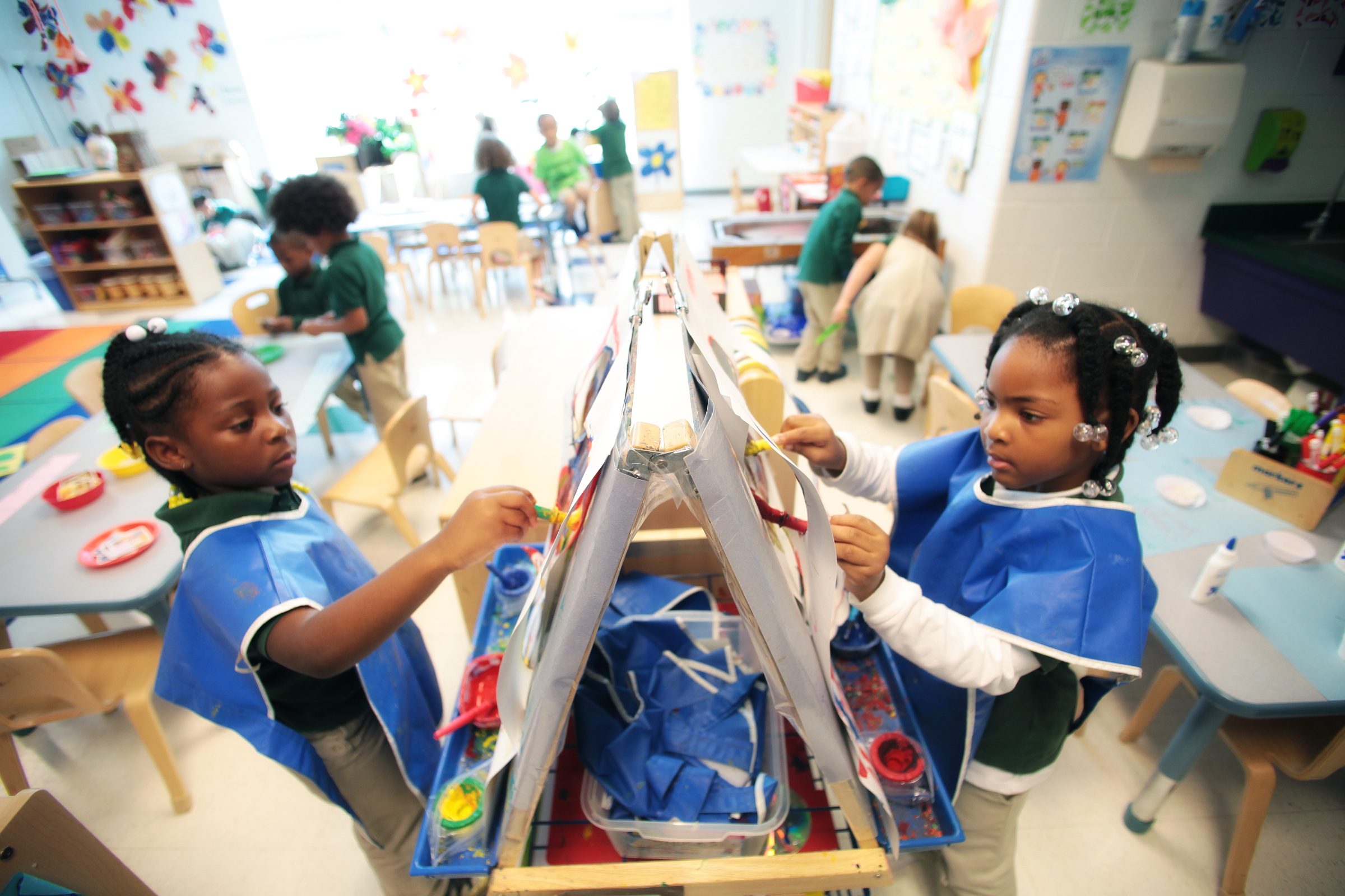 Two young students wear blue smocks as they paint a picture. The young African-American students are in a classroom at the Drew Charter School in Atlanta.