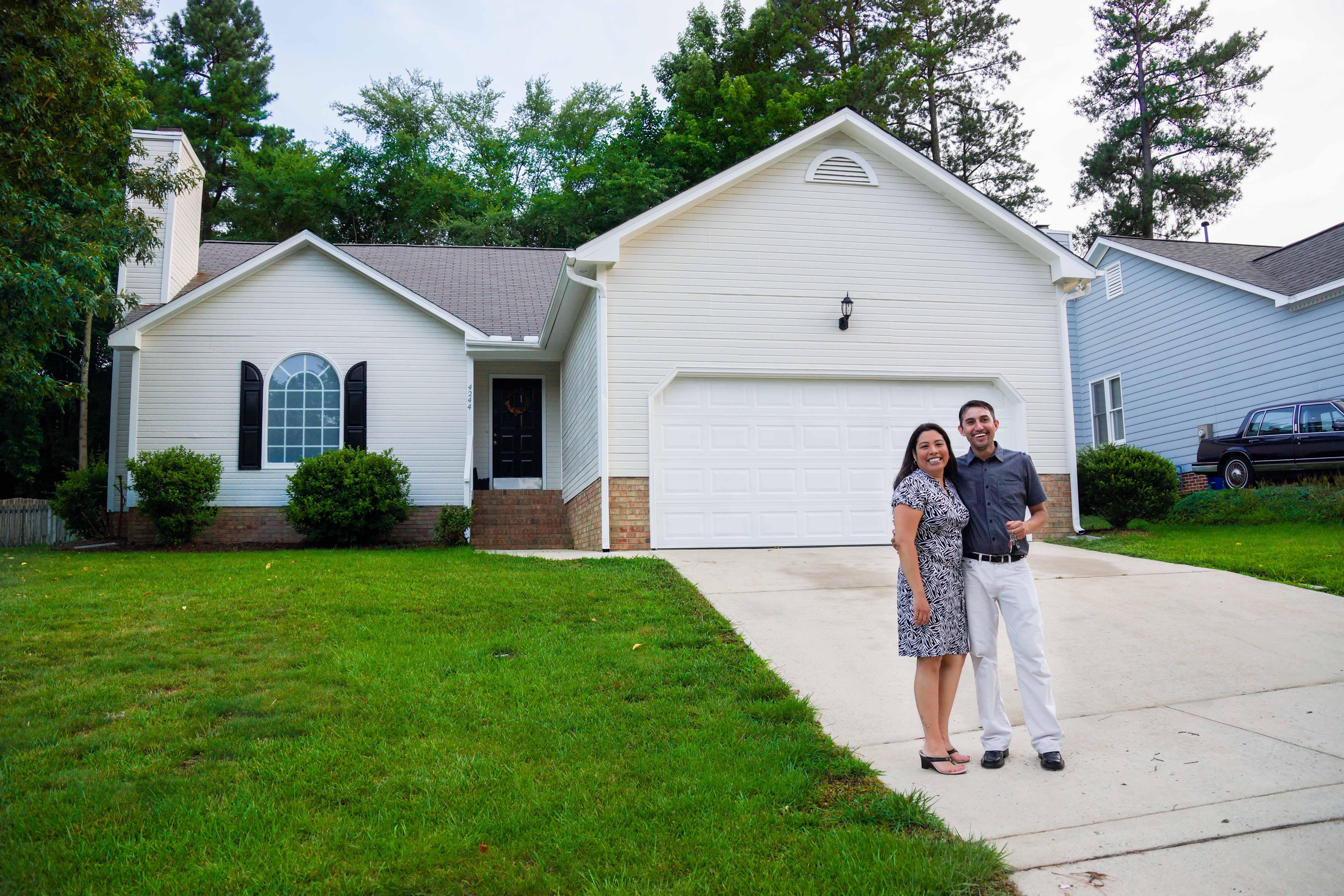 A woman and man stand together smiling in front of their new home in North Carolina. 