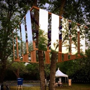 An art installation made of mirrors and wood surrounds a tree.
