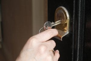 A white hand puts a silver colored key into a door lock.