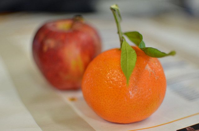 A close-up view of an apple and an orange on a table. They are bright red and orange, respectively, and the orange has a stem some green leaves. Illustrating an article about CDCs 