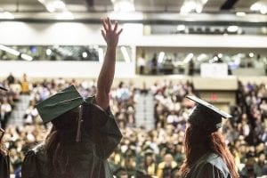Profile of a graduate in cap and gown as she waves to family in the audience.