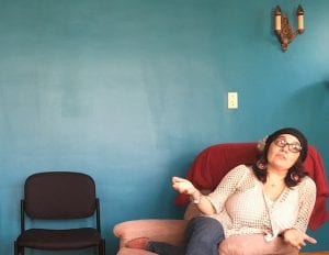 Adela Nieves sits on pink chair in front of a blue wall.