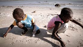 air quality: Photo shows two children, one wearing a blue shirt and other a pink shirt, playing in the sand on a beach.