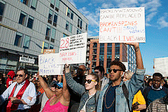 A multiracial group of people stand in a street with signs protesting Freddie Gray's death.