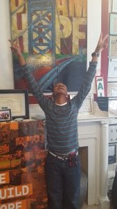 A young man who is part of a job training program in Camden, New Jersey, raises both of his arms to the air after earning a job.